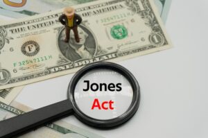 Jones Act displayed under a magnifying glass, with a background of banknotes and coins, representing basic financial concepts and business themes.