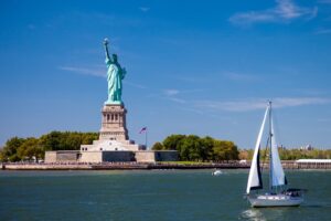 A sailboat drifts leisurely past Liberty Island, where the renowned Statue of Liberty stands.