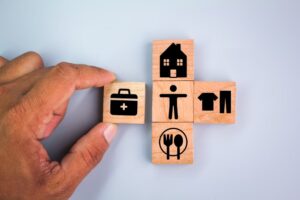 Wooden cube with icons of food, Clothing, housing, medical bag, four basic human needs concepts. 
