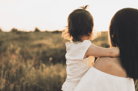 mother holding child in a sunlit field.