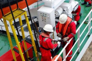 The ship's safety officer assists the crew in attaching an inflatable life vest during a man overboard drill, while a fast rescue boat is launched.