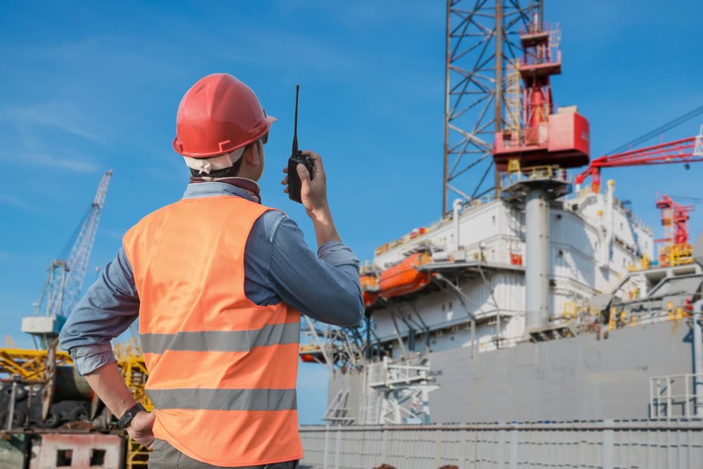 Worker holding a walkie-talkie while coordinating tasks at a shipyard.