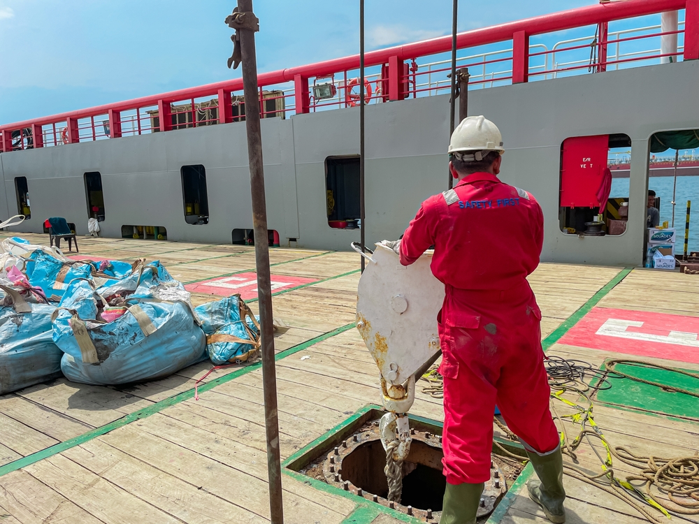 The ship's crew is conducting cargo lifting operations with a deck crane, transporting mud drilling waste to an offshore location.